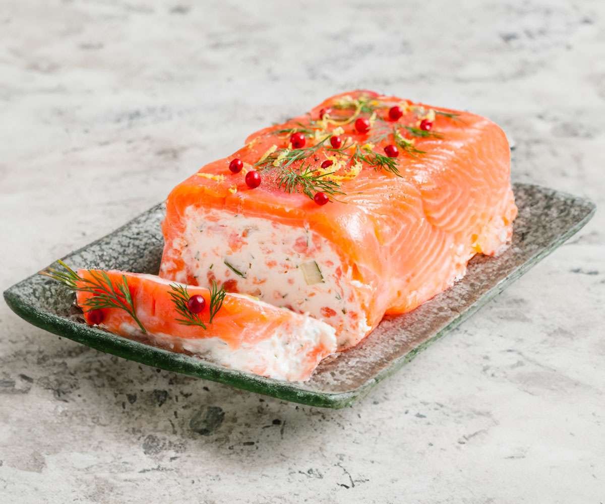 Tranches de bûche salée au saumon fumé et frais, au fromage de chèvre et concombre, décorées d’aneth et de citron vert sur un plat de fête