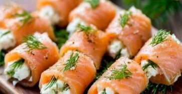 Roulés de saumon fumé garnis de fromage frais à l’aneth, coupés en bouchées et disposés sur un plateau apéritif