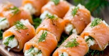 Roulés de saumon fumé garnis de fromage frais à l’aneth, coupés en bouchées et disposés sur un plateau apéritif