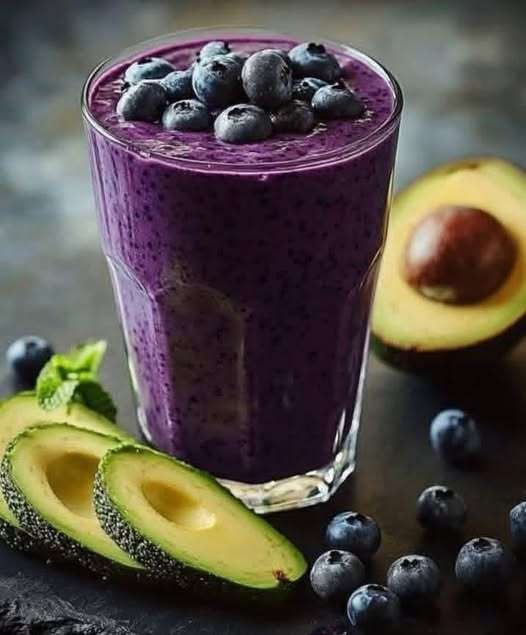 Verre de smoothie avocat-myrtilles crémeux, décoré de myrtilles fraîches et d’une tranche d’avocat.