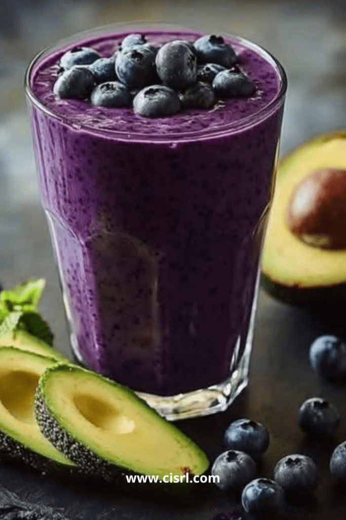 Verre de smoothie avocat-myrtilles crémeux, décoré de myrtilles fraîches et d’une tranche d’avocat.