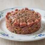 Assiette de tartare de bœuf aux câpres dressé au cercle avec échalote, cornichons et jaune d’œuf.